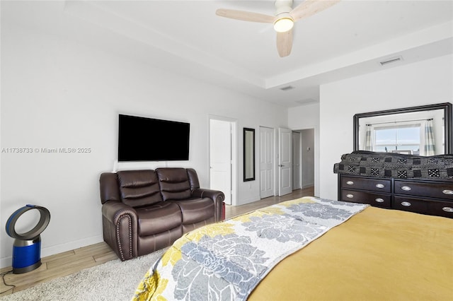 bedroom with a tray ceiling, ceiling fan, and light hardwood / wood-style flooring