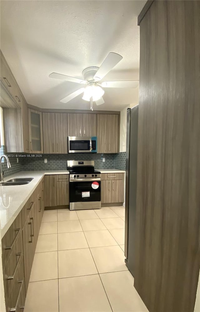 kitchen featuring sink, light tile patterned floors, appliances with stainless steel finishes, ceiling fan, and backsplash