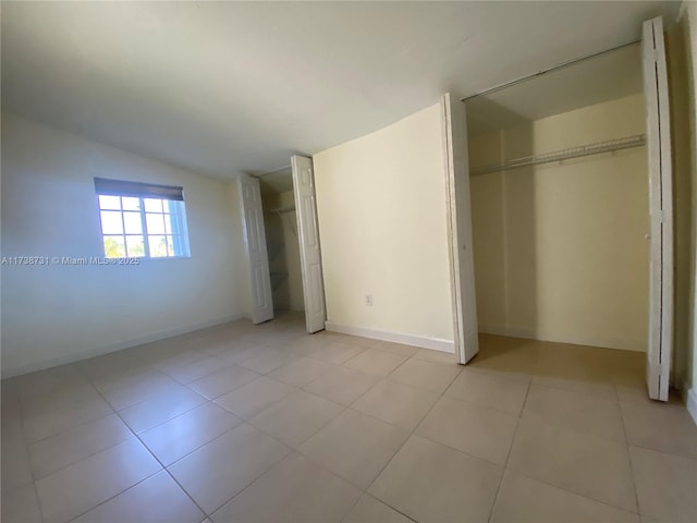 unfurnished bedroom with vaulted ceiling, two closets, and light tile patterned floors