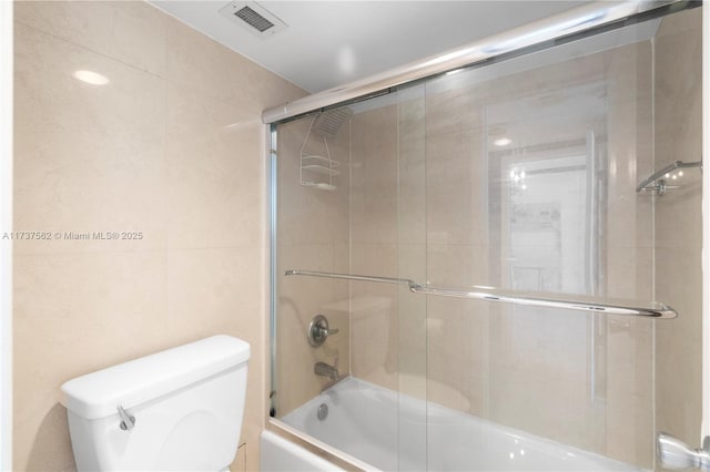 bathroom with tile walls, shower / bath combination with glass door, and toilet