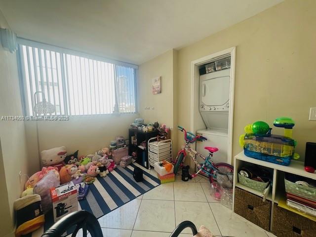 playroom with stacked washer and dryer and light tile patterned floors