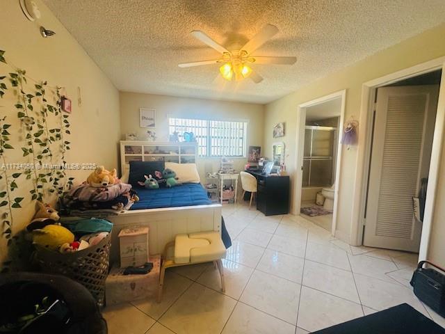 bedroom with light tile patterned flooring, connected bathroom, ceiling fan, and a textured ceiling