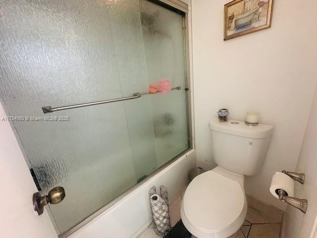 bathroom with tile patterned flooring, shower / bath combination with glass door, and toilet