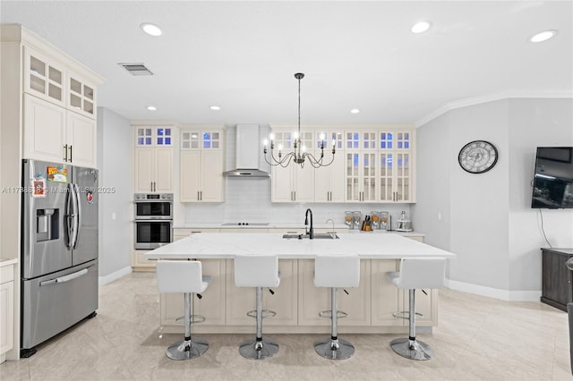 kitchen featuring stainless steel appliances, a center island with sink, wall chimney range hood, and hanging light fixtures