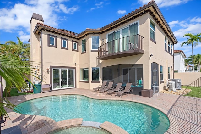 rear view of property featuring a pool with hot tub, cooling unit, a patio area, and a balcony