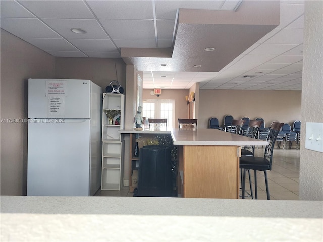 kitchen with a paneled ceiling, a kitchen breakfast bar, kitchen peninsula, white fridge, and tile patterned flooring