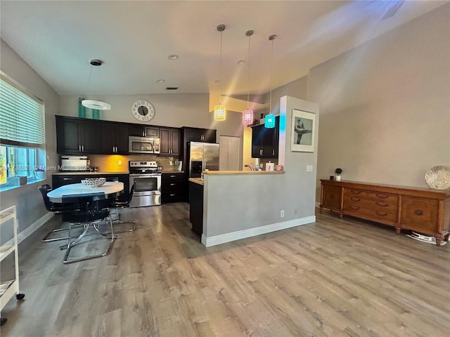 kitchen with stainless steel appliances, kitchen peninsula, hanging light fixtures, and light hardwood / wood-style flooring