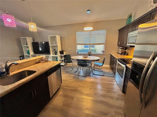 kitchen with dark brown cabinetry, sink, appliances with stainless steel finishes, pendant lighting, and light hardwood / wood-style floors