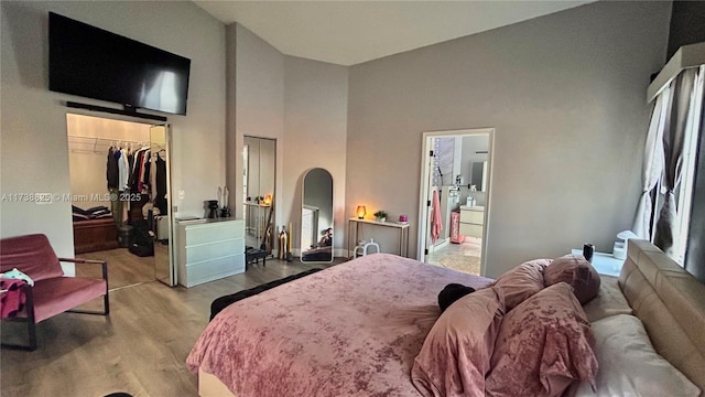 bedroom featuring ensuite bath, a walk in closet, light hardwood / wood-style floors, and a high ceiling