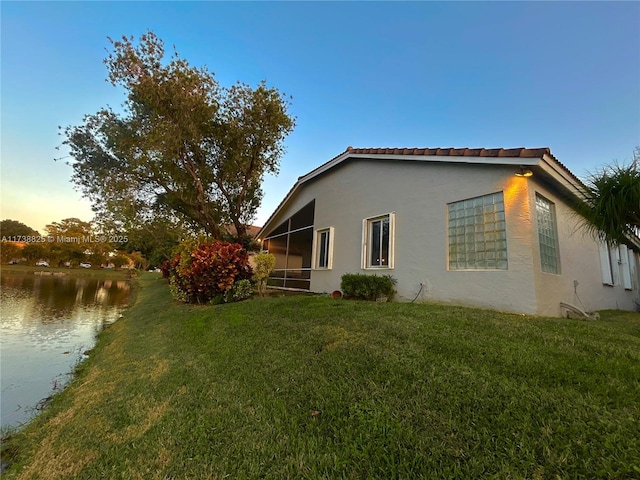 property exterior at dusk with a water view, a yard, and a sunroom