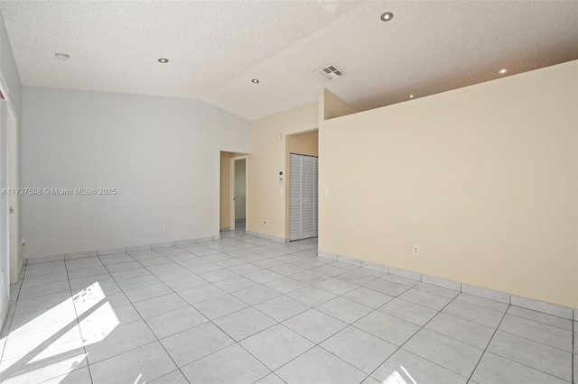 tiled empty room featuring vaulted ceiling and a textured ceiling