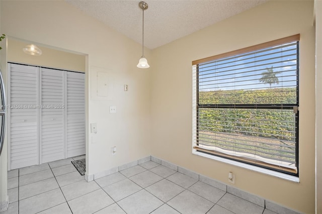 unfurnished dining area featuring light tile patterned floors, vaulted ceiling, and a textured ceiling