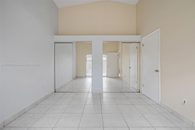 unfurnished bedroom with light tile patterned flooring, high vaulted ceiling, and two closets