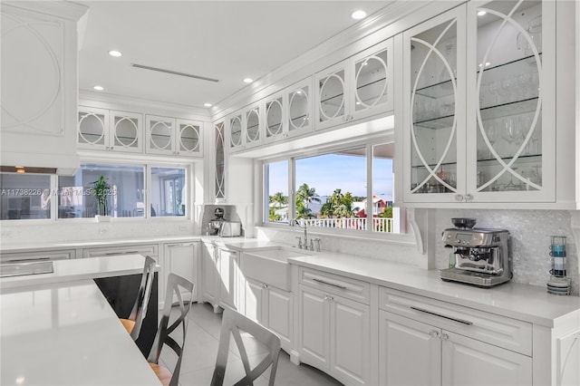 kitchen with tasteful backsplash, light tile patterned floors, sink, and white cabinets