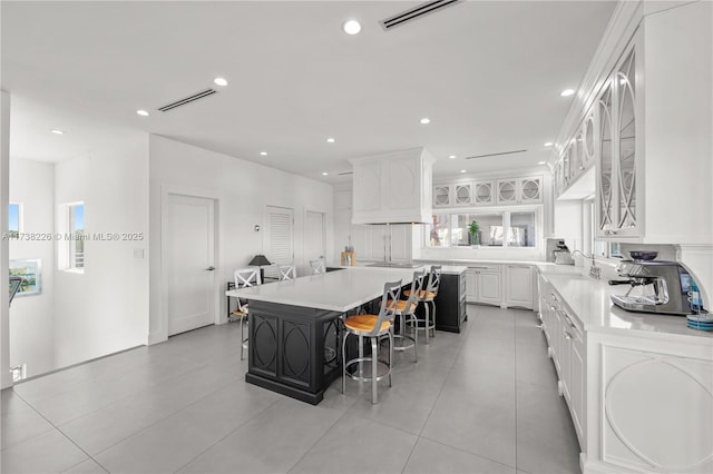 kitchen featuring premium range hood, a kitchen island, white cabinetry, a kitchen breakfast bar, and light tile patterned floors