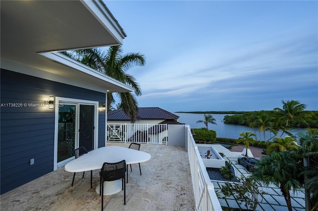 patio terrace at dusk featuring a water view and a balcony