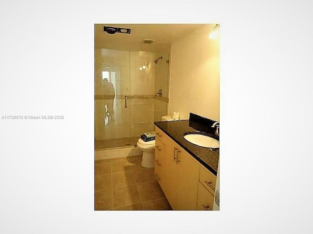 bathroom featuring tile patterned floors, vanity, toilet, and a shower with shower door