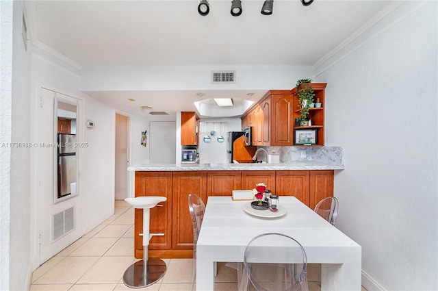 kitchen featuring light tile patterned floors, backsplash, fridge, a kitchen breakfast bar, and kitchen peninsula