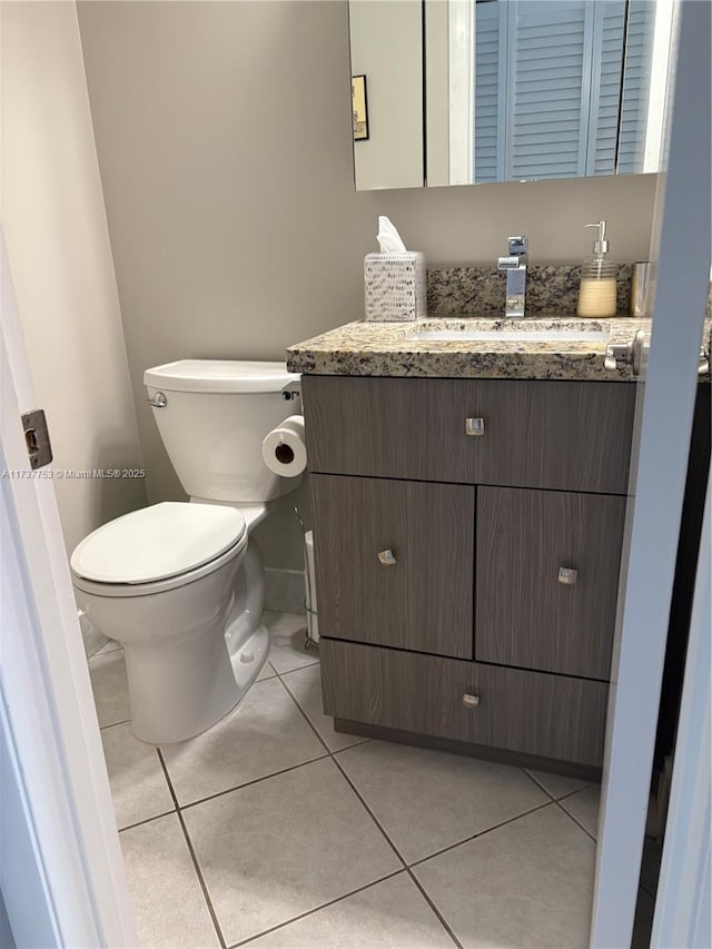 half bath with toilet, baseboards, vanity, and tile patterned floors