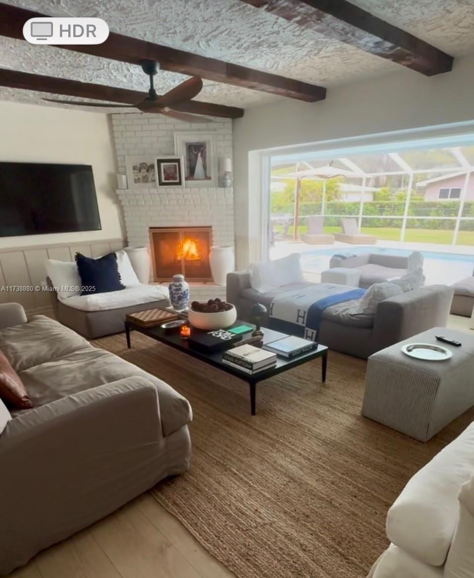 living room with a textured ceiling, beamed ceiling, ceiling fan, a fireplace, and hardwood / wood-style floors