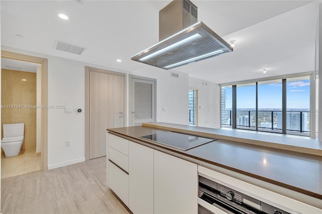 kitchen featuring island exhaust hood, black electric stovetop, oven, light hardwood / wood-style floors, and white cabinets