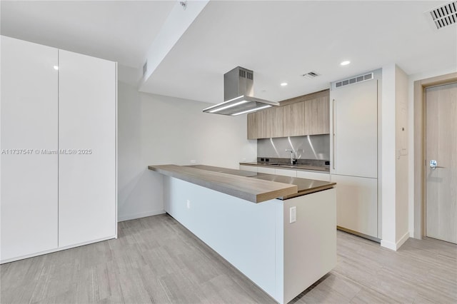 kitchen with sink, island range hood, light hardwood / wood-style flooring, black electric cooktop, and kitchen peninsula