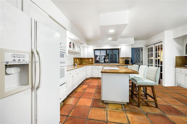 kitchen with white appliances, a breakfast bar, tasteful backsplash, white cabinets, and a kitchen island