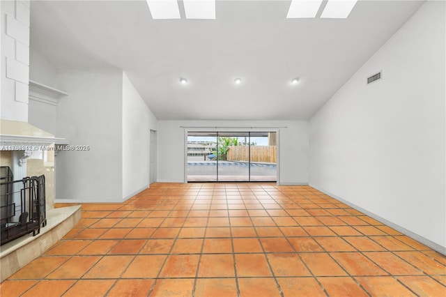 unfurnished living room with light tile patterned flooring, a skylight, and high vaulted ceiling