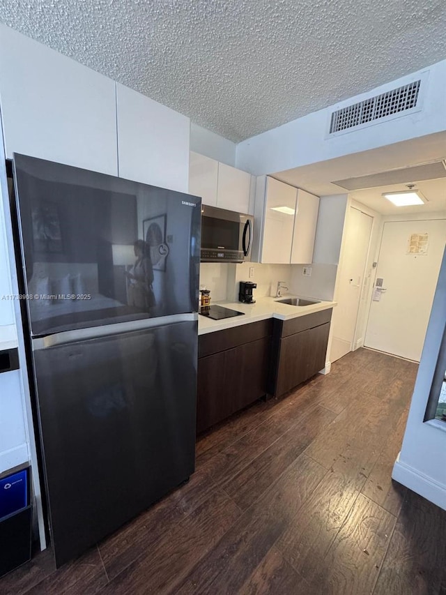 kitchen with sink, dark hardwood / wood-style floors, black appliances, a textured ceiling, and white cabinets