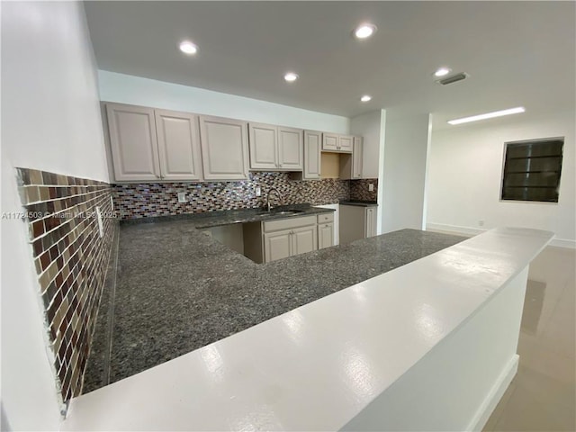 kitchen featuring sink, backsplash, dark stone counters, and kitchen peninsula