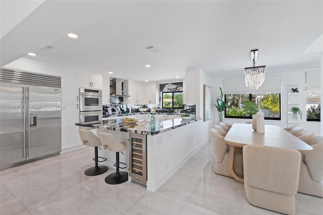 kitchen featuring stainless steel appliances, a peninsula, white cabinetry, hanging light fixtures, and dark stone counters