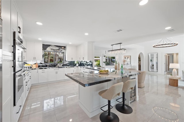 kitchen featuring decorative light fixtures, visible vents, an inviting chandelier, white cabinetry, and a kitchen breakfast bar