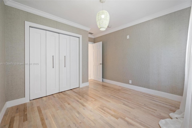 unfurnished bedroom featuring a closet, light wood-style flooring, ornamental molding, baseboards, and wallpapered walls