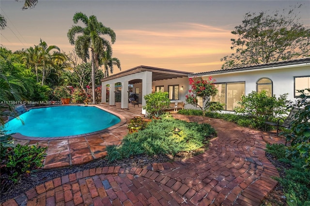 pool at dusk with a patio area and an outdoor pool