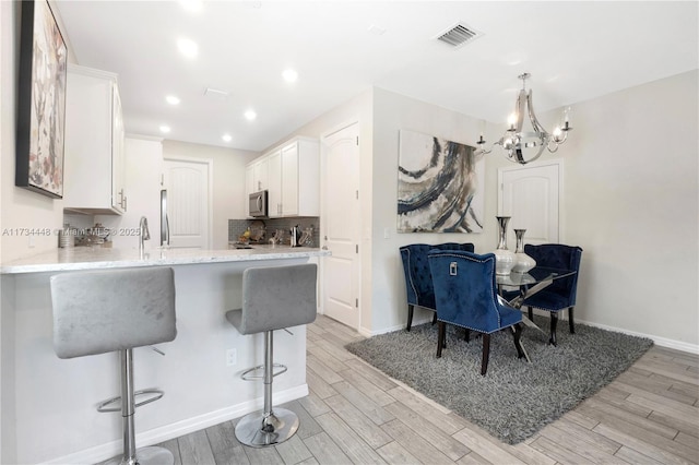 kitchen featuring a breakfast bar, white cabinetry, decorative backsplash, kitchen peninsula, and light wood-type flooring