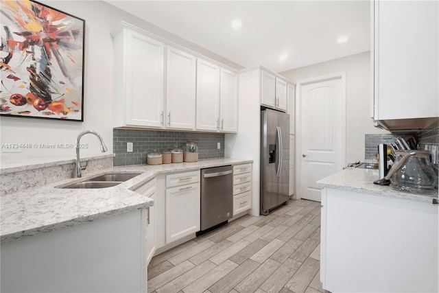 kitchen with sink, light stone counters, light wood-type flooring, stainless steel appliances, and white cabinets