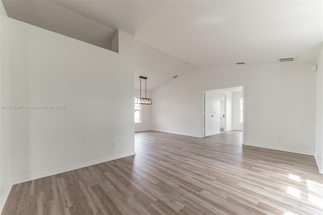 unfurnished room featuring light wood-style floors, visible vents, vaulted ceiling, and baseboards