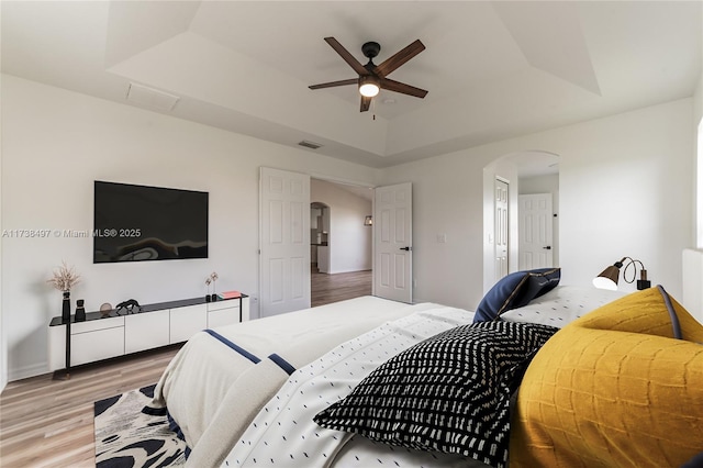 bedroom featuring light hardwood / wood-style floors, a raised ceiling, and ceiling fan