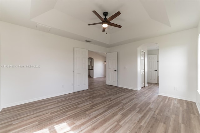 spare room with ceiling fan, light wood-type flooring, and a tray ceiling