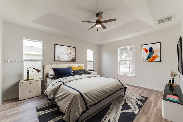 bedroom with light hardwood / wood-style flooring, ceiling fan, and a tray ceiling