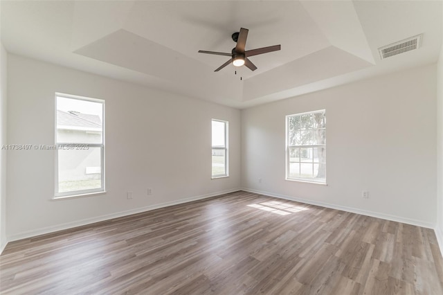 empty room featuring light wood finished floors, baseboards, visible vents, and a raised ceiling