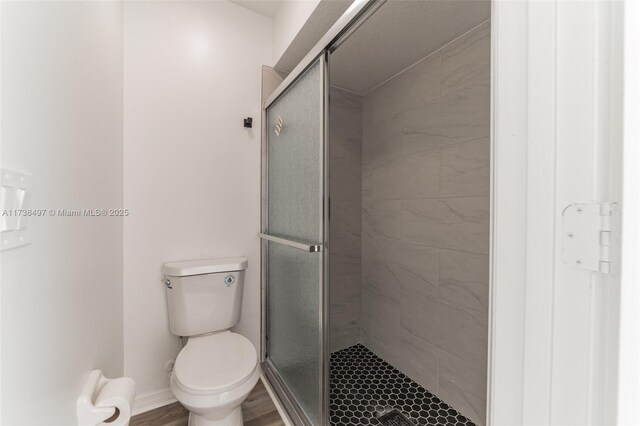 bathroom with hardwood / wood-style flooring, toilet, and a shower with shower door