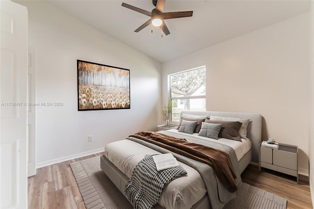 bedroom with a ceiling fan, vaulted ceiling, light wood-style flooring, and baseboards