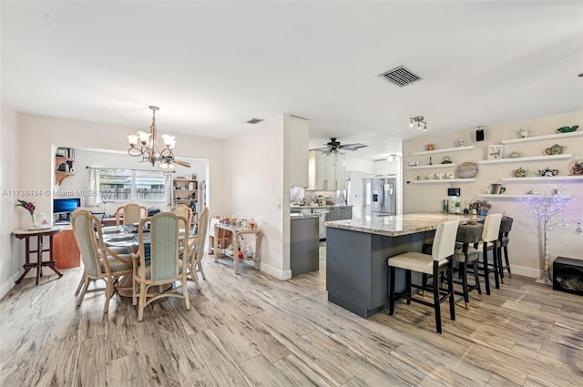 kitchen featuring pendant lighting, light stone counters, stainless steel fridge, and light hardwood / wood-style flooring