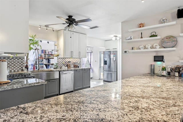 kitchen featuring light stone counters, decorative backsplash, gray cabinets, and stainless steel appliances