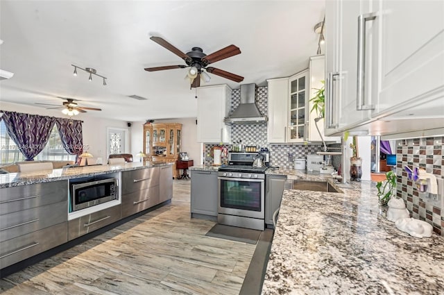 kitchen featuring white cabinetry, backsplash, stainless steel appliances, light stone countertops, and wall chimney exhaust hood