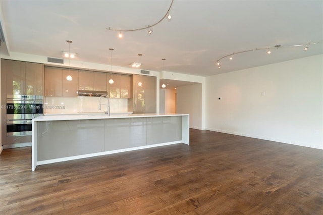 kitchen featuring a large island with sink, dark hardwood / wood-style floors, double oven, and decorative light fixtures