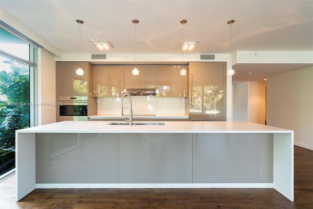 kitchen featuring decorative light fixtures, oven, and a large island with sink