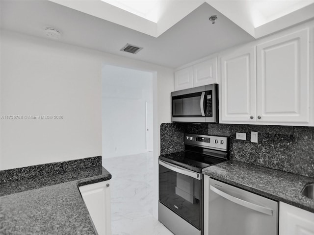 kitchen with white cabinetry, backsplash, stainless steel appliances, and dark stone countertops