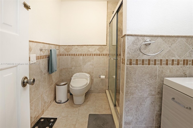 bathroom with a shower with door, tile walls, tile patterned flooring, vanity, and toilet